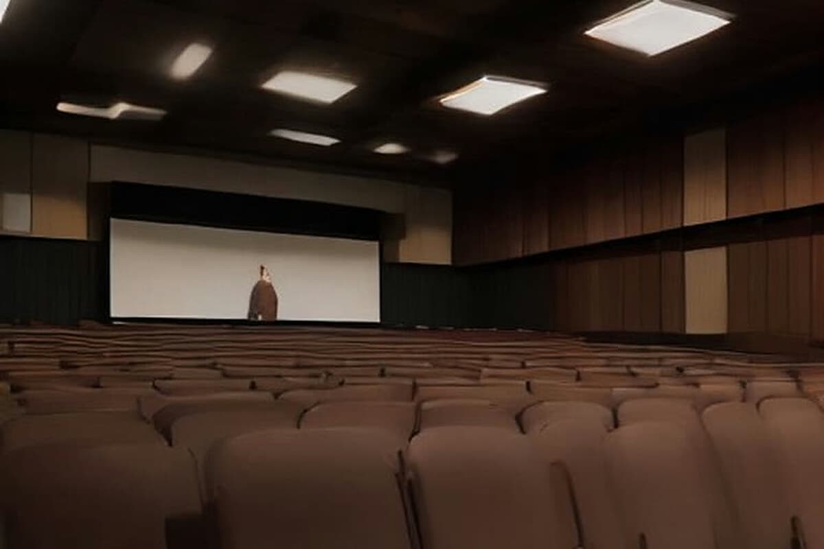 Konferans salonunda sıralara oturmuş imam hatip öğrencisi gibi gençler, önde boş bir kürsü ve sahne ışıkları; dinleyiciler arkadan görünüyor, yüzleri seçilmiyor.